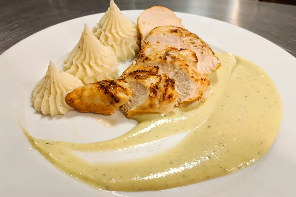 Sliced Chicken Steak with Blue Cheese Sauce on a white plate with mashed potato quenelles.