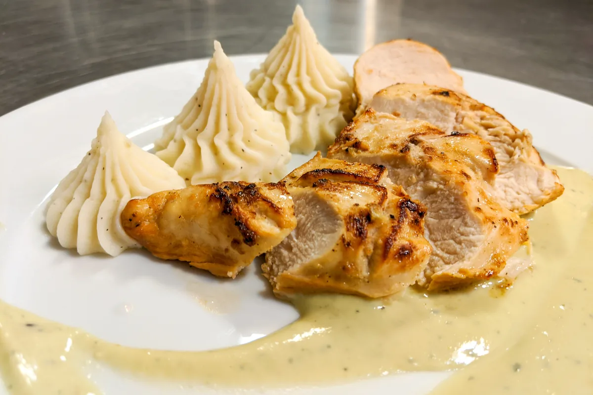 Sliced Chicken Steak with Blue Cheese Sauce beside piped mashed potato swirls on a white plate