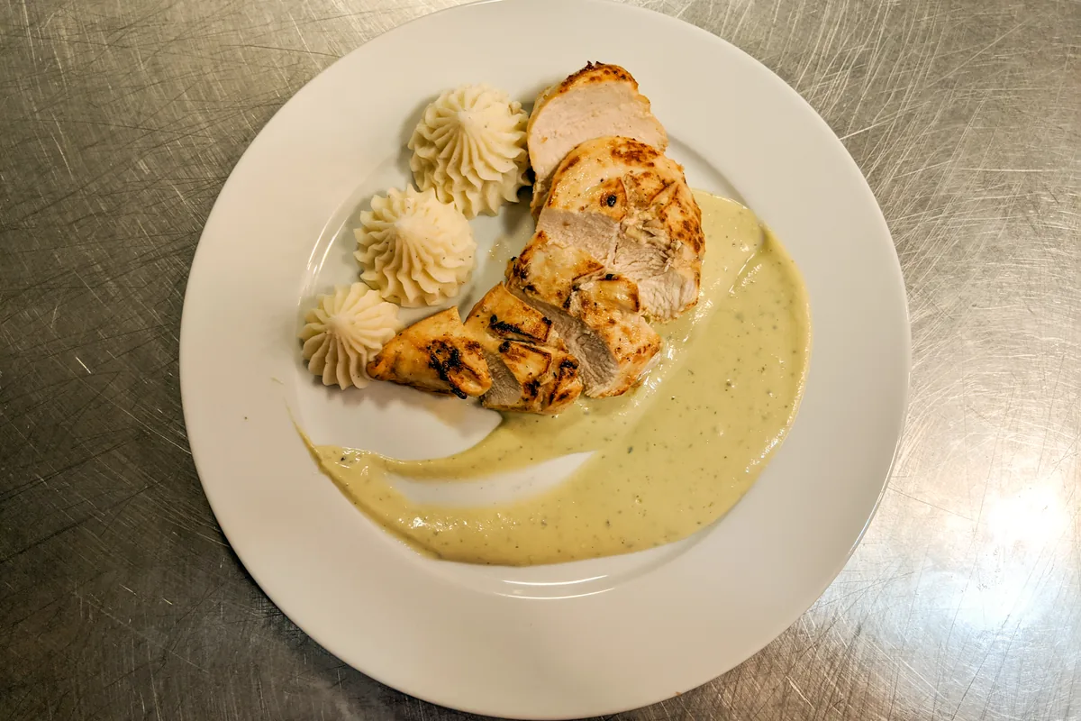 Sliced Chicken Steak with Blue Cheese Sauce on a white plate with piped mashed potato swirls.