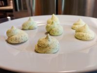 Seven piped mounds of pale green herb butter arranged on a white plate.