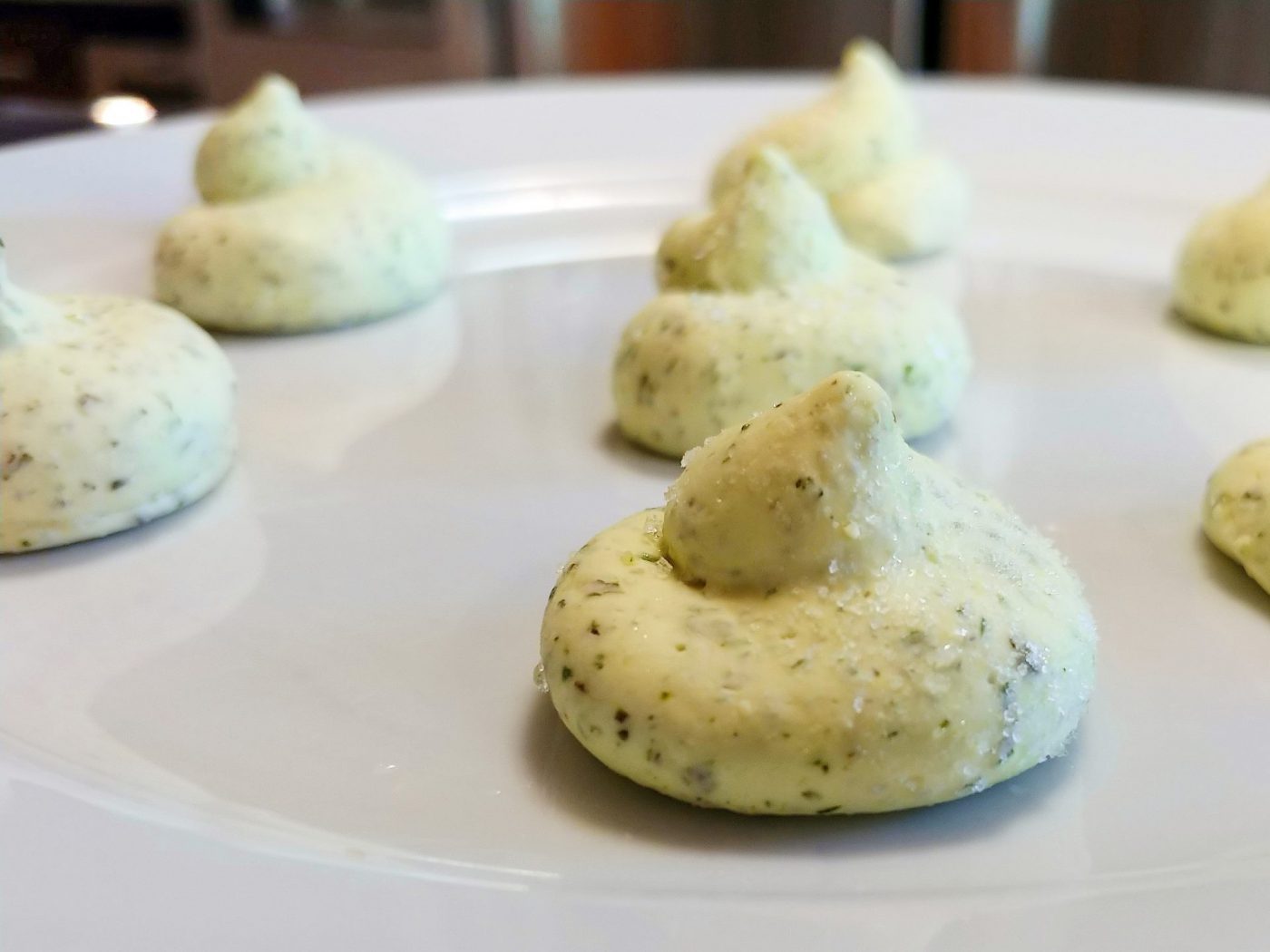 Small dollops of pale green Herb Butter with herb flecks arranged on a white ceramic plate.