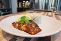 Blackened Salmon Blackened Salmon fillet with a lemon wedge and herb garnish beside herbed rice on a white plate