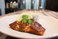 Blackened Salmon Blackened Salmon fillet with a lemon wedge and parsley garnish beside herbed rice on a white plate.