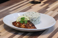 Blackened Salmon Blackened Salmon fillet with a lemon wedge and herb sprig beside herbed white rice on a plate.