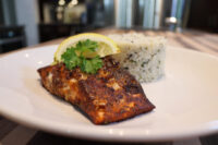 Blackened Salmon Blackened Salmon fillet with lemon wedge and parsley, served beside herbed rice on a white plate.