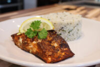 Blackened Salmon Blackened Salmon fillet with a lemon wheel and parsley beside herbed rice on a white plate