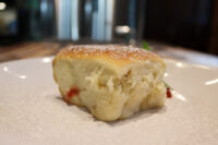 A golden Buchty (Czech sweet filled bun) dusted with powdered sugar, red filling visible at its base, on a white plate.