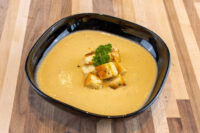 Cauliflower Soup A black bowl of creamy Cauliflower Soup topped with golden croutons and a parsley sprig.