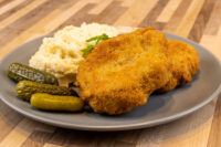 Golden breaded Dutch Schnitzel (Holandský Řízek) on a grey plate with mashed potato and pickles