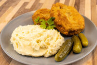 Two golden breaded Dutch Schnitzel (Holandský Řízek) cutlets on a grey plate with mashed potatoes and pickles.