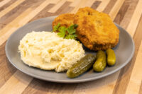 Two breaded fried Dutch Schnitzel (Holandský Řízek) cutlets with mashed potatoes, parsley, and pickles.