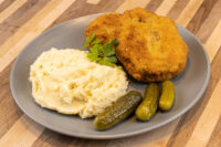 Golden fried Dutch Schnitzel (Holandský Řízek) with mashed potatoes, parsley, and pickles on a gray plate.