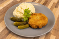 Golden breaded Dutch Schnitzel (Holandský Řízek) on a gray plate with mashed potatoes and gherkins.