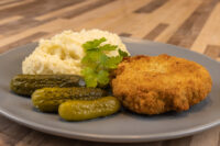 Golden breaded Dutch Schnitzel (Holandský Řízek) with mashed potatoes, pickles, and parsley on a gray plate