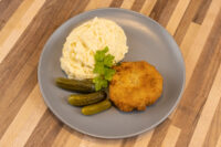 Golden breaded Dutch Schnitzel (Holandský Řízek) on a gray plate with mashed potatoes, pickles, and parsley.