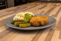 Golden breaded Dutch Schnitzel (Holandský Řízek) on a grey plate with mashed potatoes and pickles.