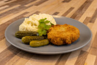 Golden breaded Dutch Schnitzel (Holandský Řízek) plated with mashed potatoes, cornichons, and parsley.