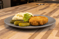 Golden breaded Dutch Schnitzel (Holandský Řízek) on a grey plate with mashed potato and pickles.