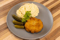 Golden breaded Dutch Schnitzel (Holandský Řízek) on a grey plate with mashed potatoes and gherkins.