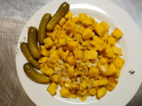 Plate of diced Fried Dumplings with onion and spice coating, served with four whole dill pickles.