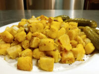 Plate of golden diced Fried Dumplings with crispy browned edges, served with two whole dill pickles