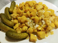 Diced Fried Dumplings coated in egg with chopped onion and pepper, plated with whole dill pickles