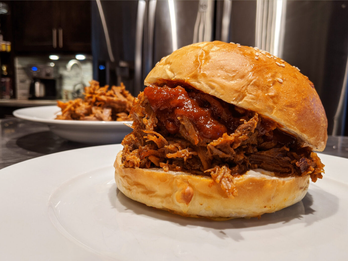 Pulled pork piled high on a sesame bun with barbecue sauce, on a white plate