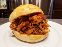 Pulled pork piled high in a bread roll with red barbecue sauce, on a white plate
