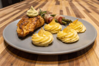 Seared Rosemary Chicken Breasts with herb sauce, duchess potatoes, and bacon-wrapped asparagus on a grey plate.