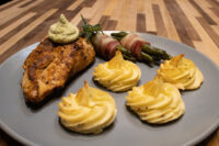 Seared Rosemary Chicken Breasts topped with herb cream, rosemary sprig, potatoes and asparagus on grey plate