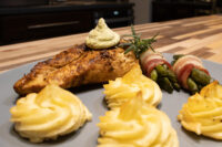 Seared Rosemary Chicken Breasts topped with herb cream, plated with duchess potatoes and bacon-wrapped asparagus.