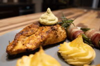 Seared Rosemary Chicken Breasts with green sauce, piped potato, and bacon-wrapped asparagus on a grey plate