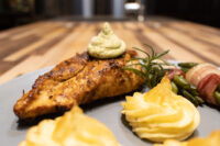 Seared Rosemary Chicken Breast with herb cream, duchess potatoes, and bacon-wrapped asparagus on a grey plate.