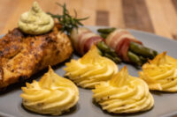 Seared Rosemary Chicken Breasts topped with green sauce, served with potato swirls and bacon-wrapped asparagus.