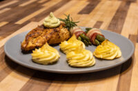 Seared Rosemary Chicken Breasts topped with herb cream, served with duchess potatoes and bacon-wrapped asparagus.