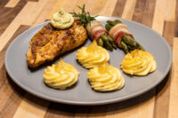 Seared Rosemary Chicken Breasts topped with herb butter and rosemary, served with asparagus and potato swirls.