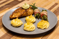 Seared Rosemary Chicken Breast topped with herb butter, served with duchess potatoes and bacon-wrapped asparagus.