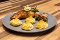 Seared Rosemary Chicken Breasts topped with herb sauce, served with duchess potatoes and bacon-wrapped asparagus.