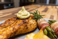 Seared Rosemary Chicken Breasts topped with herb cream, rosemary sprig, and bacon-wrapped green beans on a plate.