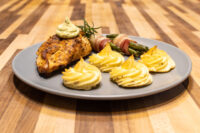 Seared Rosemary Chicken Breast topped with green herb sauce, served with duchess potatoes and bacon-wrapped vegetables.
