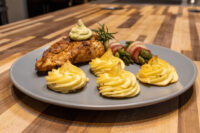 Rosemary Chicken Breasts topped with herb sauce and rosemary sprig, served with duchess potatoes and bacon-wrapped asparagus.
