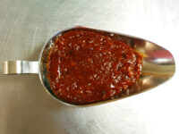 BBQ Sauce Thick red-brown BBQ Sauce piled in a metal scoop on a stainless steel surface.
