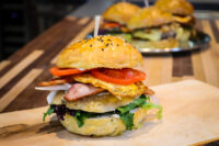 Burger Buns Sesame and black seed topped Burger Buns holding egg, bacon, tomato and greens, second burger visible behind.