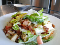 Caesar Salad with romaine, bacon, croutons, shaved cheese, and a gravy boat of dressing.