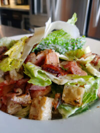 Bowl of Caesar Salad with romaine, croutons, shaved parmesan, and crispy bacon pieces