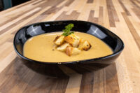 Cauliflower Soup Black bowl of creamy Cauliflower Soup topped with croutons and parsley on a wood table.