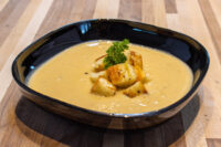 Cauliflower Soup Bowl of Cauliflower Soup topped with crispy croutons and a parsley garnish on a wooden table.