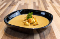 Cauliflower Soup Bowl of creamy Cauliflower Soup topped with roasted potato cubes and a parsley sprig on a wood table.