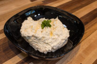 Cheese – Garlic Dip and Spread mounded in a black bowl with visible corn kernels and a parsley sprig.