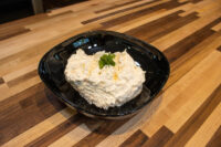 Creamy Cheese – Garlic Dip and Spread in a black bowl, garnished with herbs, on a wood counter.
